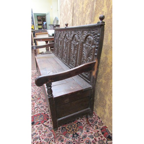 1454 - An antique oak box settle with repeating carved detail, the seat incorporating a rising lid, 185cm l... 