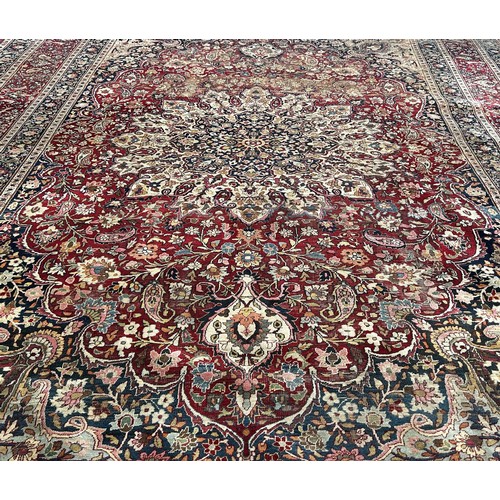 1744 - A large Middle Eastern country house carpet with an all over floral pattern on a predominantly red g... 