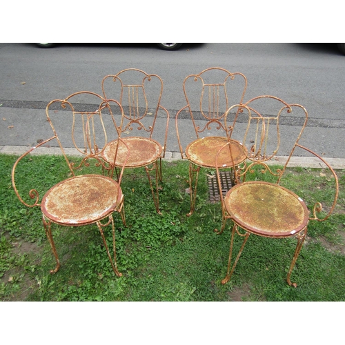 1005 - A set of four decorative weathered ironwork garden chairs the open scrollwork frames with lyre shape... 