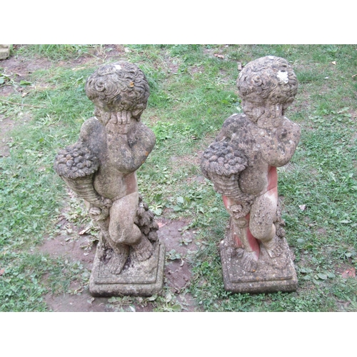 1021 - A matched pair of cast composition stone garden ornaments in the form of standing cherubs clutching ... 