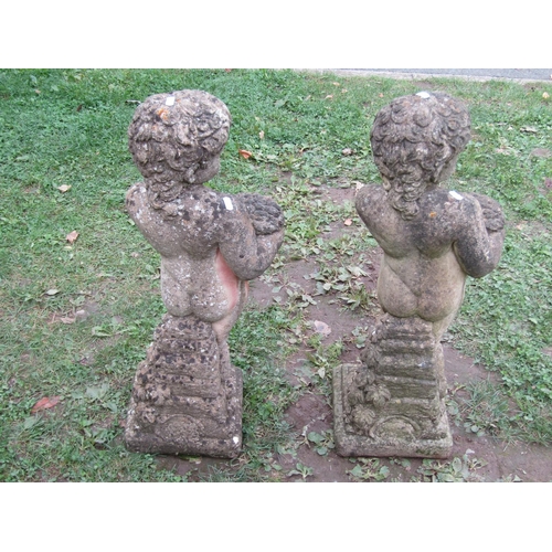 1021 - A matched pair of cast composition stone garden ornaments in the form of standing cherubs clutching ... 