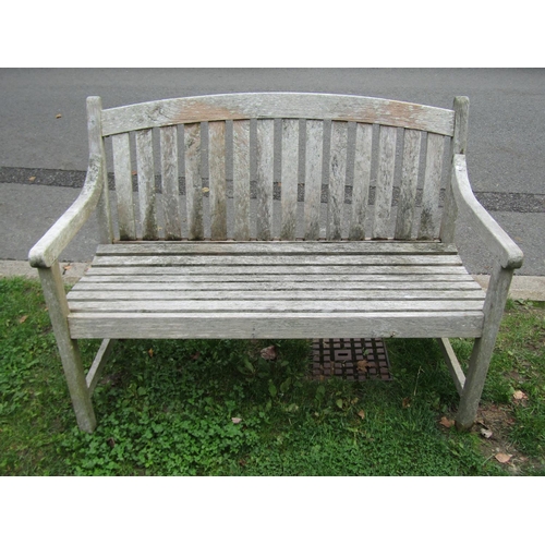 1051 - A weathered teak two seat garden bench with slatted seat and back beneath an arched rail, 120 cm wid... 