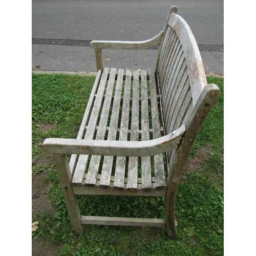 1051 - A weathered teak two seat garden bench with slatted seat and back beneath an arched rail, 120 cm wid... 