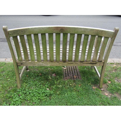 1051 - A weathered teak two seat garden bench with slatted seat and back beneath an arched rail, 120 cm wid... 