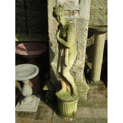 1027 - A weathered cast composition stone garden statue of a standing scantily dressed classical maiden rai... 