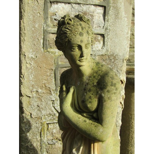 1027 - A weathered cast composition stone garden statue of a standing scantily dressed classical maiden rai... 