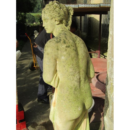 1027 - A weathered cast composition stone garden statue of a standing scantily dressed classical maiden rai... 