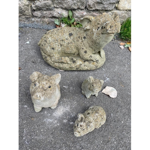 1094 - Four weathered cast composition stone garden ornaments in the for of pigs in various poses, the larg... 