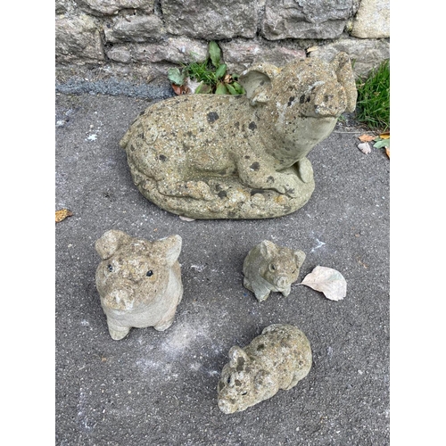 1094 - Four weathered cast composition stone garden ornaments in the for of pigs in various poses, the larg... 