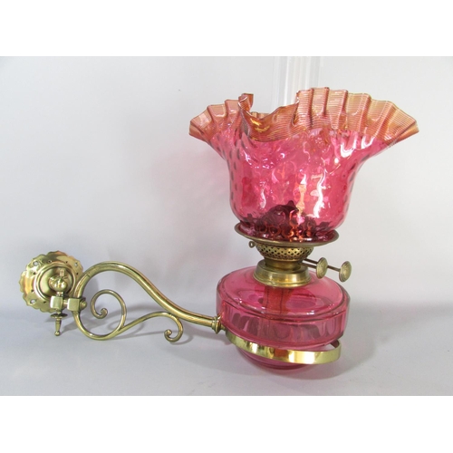 605 - A Victorian brass wall bracketed oil lamp with a crimped Cranberry glass shade and font.