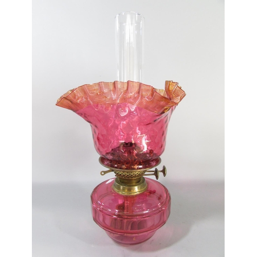 605 - A Victorian brass wall bracketed oil lamp with a crimped Cranberry glass shade and font.