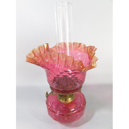 605 - A Victorian brass wall bracketed oil lamp with a crimped Cranberry glass shade and font.