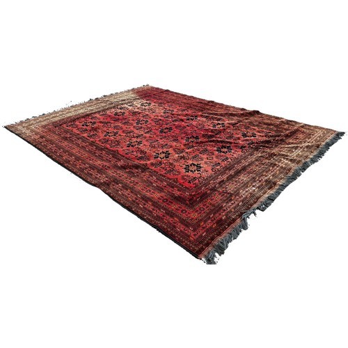 1702 - A large Middle Eastern carpet with an all over geometric pattern on a red ground, very faded in plac... 