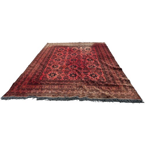 1702 - A large Middle Eastern carpet with an all over geometric pattern on a red ground, very faded in plac... 