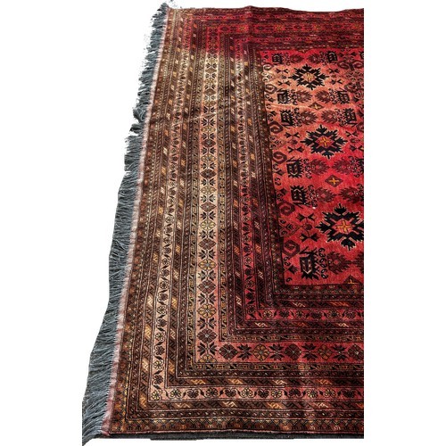 1702 - A large Middle Eastern carpet with an all over geometric pattern on a red ground, very faded in plac... 