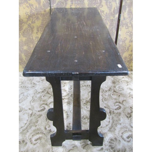 1129 - A dark stained oak table, the rectangular top raised on shaped supports united by a central through ... 