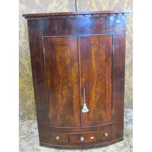 1138 - An early 19th century mahogany bow fronted hanging corner cupboard enclosed by two doors over one re... 