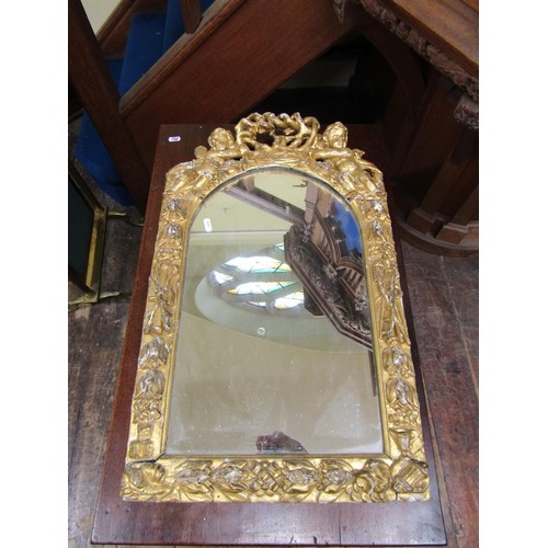 1440 - An 18th century carved pine and gilded wall mirror of arched outline showing cherubs, floral bands, ... 