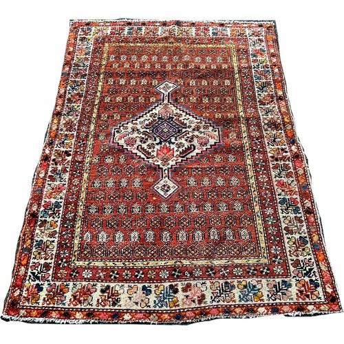 1737 - A worn Persian rug with an extended lozenge medallion on a brick red field 120 x 170cm