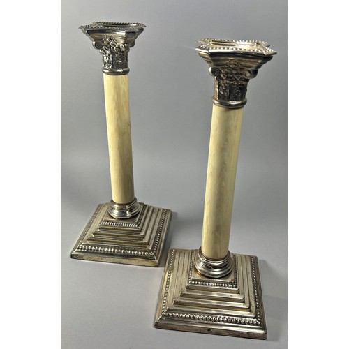 255 - A pair of faux ivory Corinthian column candlesticks, raised on a square stepped base, 30cm tall