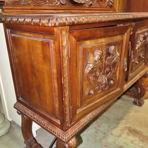 1169 - A continental walnut buffet with raised back over a pair of panelled doors with carved, mask cornuco... 