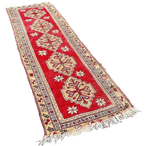 6004 - A Turkey runner with five interlocking medallions on a red ground 285cm x 90cm approximately