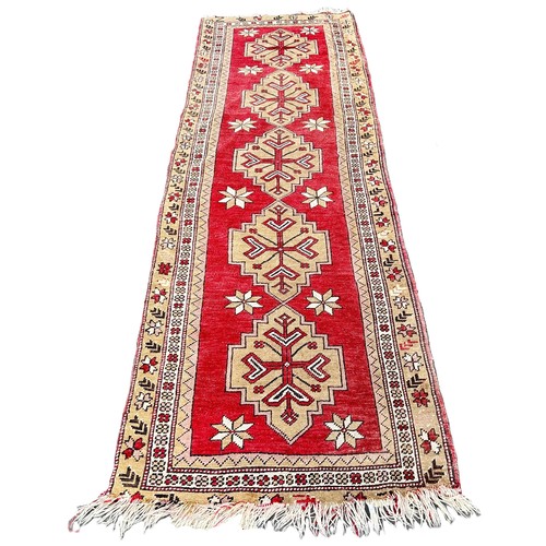 6004 - A Turkey runner with five interlocking medallions on a red ground 285cm x 90cm approximately