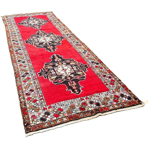 6016 - An Anatolian Turkish runner with three lozenged shaped medallions on a red ground ,410cm x 134cm