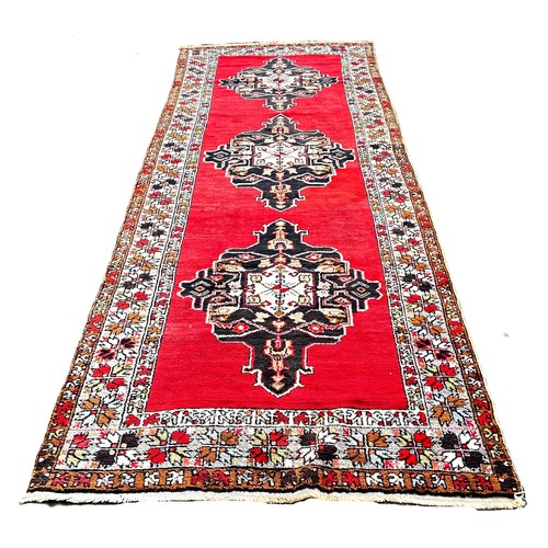 6016 - An Anatolian Turkish runner with three lozenged shaped medallions on a red ground ,410cm x 134cm