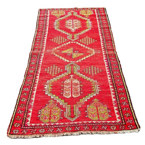 6036 - A Caucasian antique rug with triple motifs on a red ground 218 x 103 cm