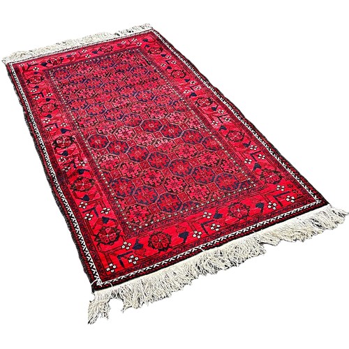 6040 - A Vintage Balouch rug with an allover geometric design on a red ground 183 x 99 cm approximately