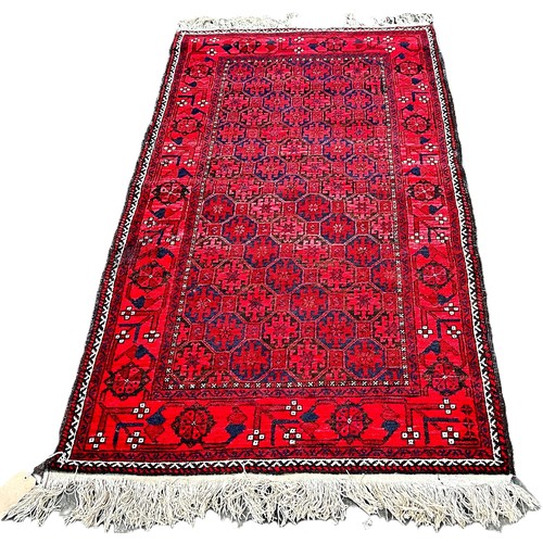 6040 - A Vintage Balouch rug with an allover geometric design on a red ground 183 x 99 cm approximately