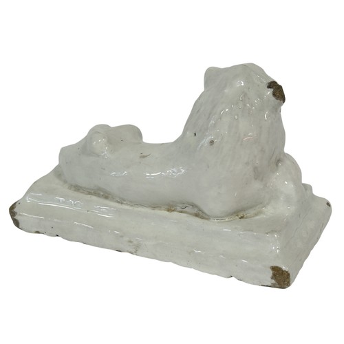 63 - A 19th century white glazed stoneware figure of a lion in a recumbent pose in, 19cm long