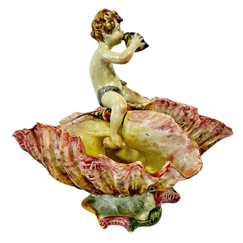 50 - A Italian Majolica table centre in the form of a young boy blowing a conch shell astride an open cla... 