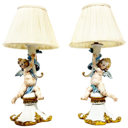 46 - A pair of Capodimonte porcelain candlesticks in the form of cherubs holding aloft a cornucopia later... 