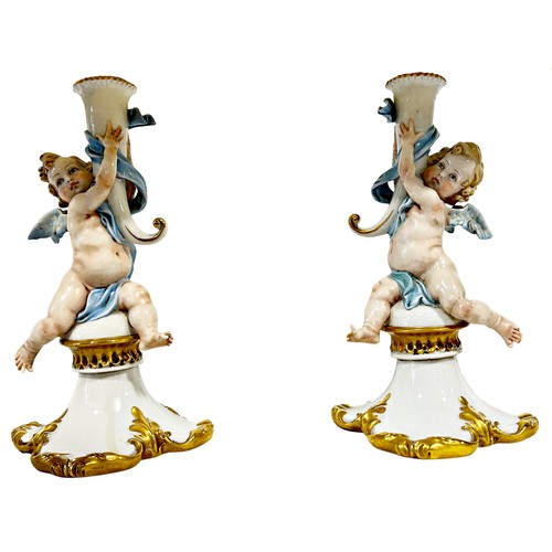 46 - A pair of Capodimonte porcelain candlesticks in the form of cherubs holding aloft a cornucopia later... 