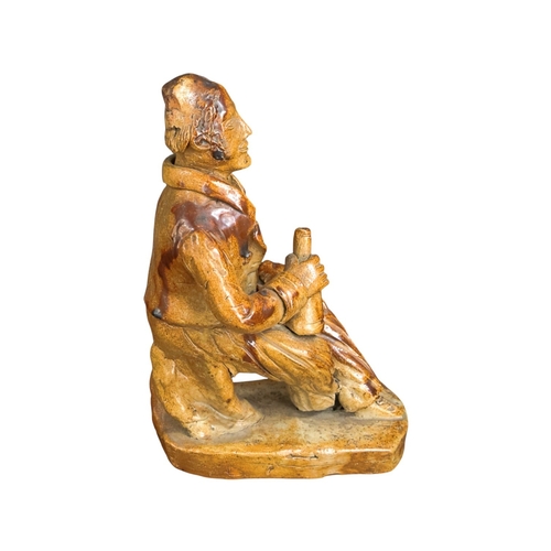 257 - An early 19th C Salt glazed figure of a seated character holding a bottle 19cm High