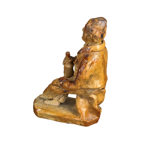 257 - An early 19th C Salt glazed figure of a seated character holding a bottle 19cm High