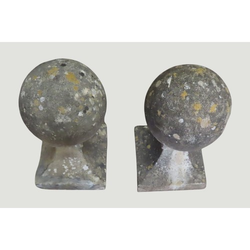 A pair of weathered composition stone sphere pier cap finials raised on ...