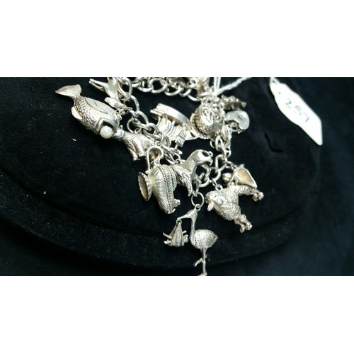 257 - A silver charm bracelet with 19 charms – the bracelet is silver. Some charms are stamped silve... 