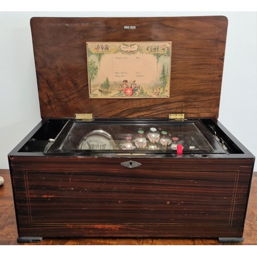 A Very Good Quality Swiss Antique Music Box. The musical movement features a drum and an array of 6 engraved bells struck by a selection of butterfly and flower strikers. All contained within an inlaid rosewood cabinet.