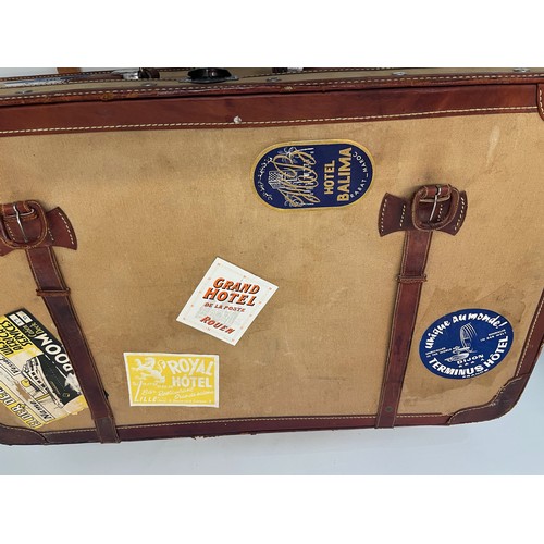 333 - Leather trimmed suitcase, with securing straps and a collection of baggage labels attached. 74 cm x ... 