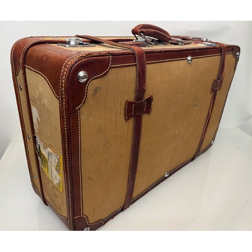 333 - Leather trimmed suitcase, with securing straps and a collection of baggage labels attached. 74 cm x ... 