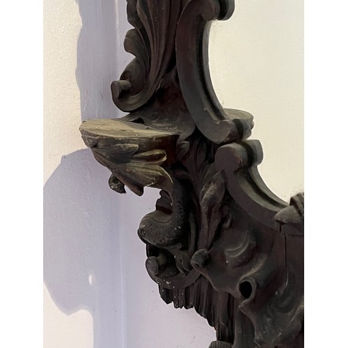 45 - A Black Forest hand carved wall mirror with two small shelves, 64 cm high x 34 cm wide.

This lot is... 