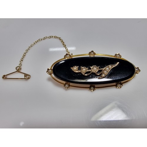 411 - A vintage 9ct yellow gold brooch inset with a large oval black onyx stone with a floral and split se... 