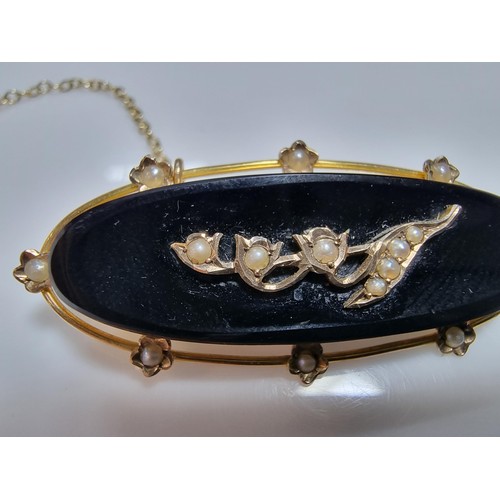 411 - A vintage 9ct yellow gold brooch inset with a large oval black onyx stone with a floral and split se... 