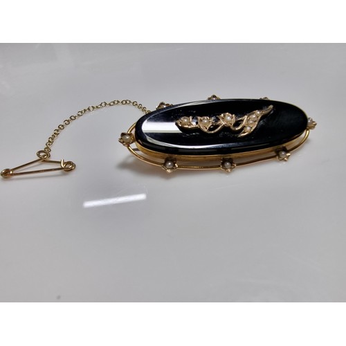 411 - A vintage 9ct yellow gold brooch inset with a large oval black onyx stone with a floral and split se... 