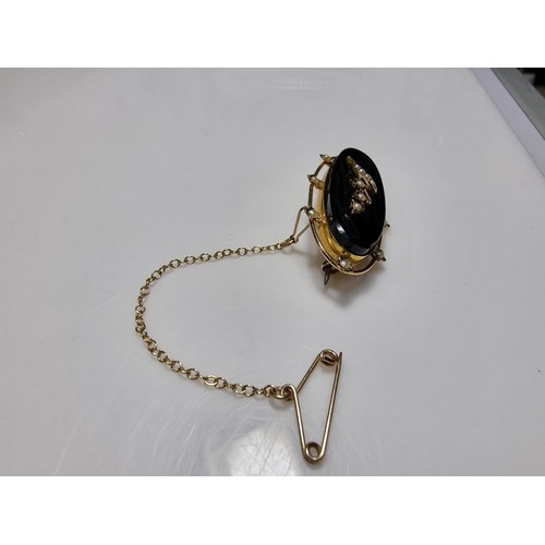 411 - A vintage 9ct yellow gold brooch inset with a large oval black onyx stone with a floral and split se... 