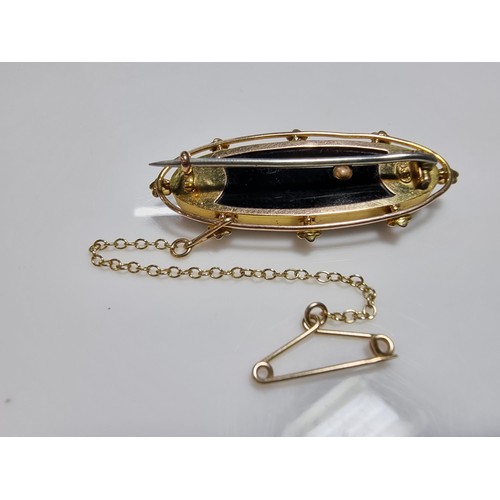 411 - A vintage 9ct yellow gold brooch inset with a large oval black onyx stone with a floral and split se... 