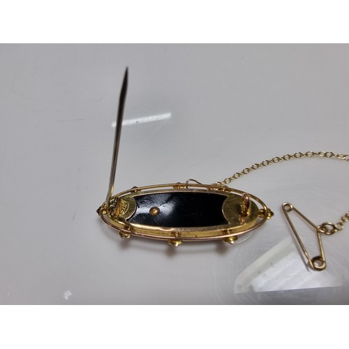 411 - A vintage 9ct yellow gold brooch inset with a large oval black onyx stone with a floral and split se... 